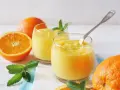 Dwa szklanki orzeźwiającego, gęstego **orange curd** z miętą i świeżymi pomarańczami.