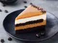 Wyśmienity kawałek tortu z warstwami brownie, kremu i karmelową polewą, ozdobiony czekoladową posypką i ziarnami kawy.