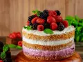 Pyszny tort z warstwami biszkoptu i kremu malinowego, ozdobiony świeżymi malinami, jeżynami i miętą.