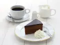 Pyszny tort Sachera z bitą śmietaną i kawą na białym drewnianym stole. Idealny deser na chwilę relaksu.