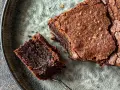 Pyszne, wilgotne brownie bezglutenowe na popękanym, szarym talerzu. Kawałek z widelcem czeka na spróbowanie.