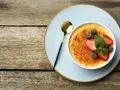 Idealny creme brulee przepis na deser. Karmelizowana skórka, świeże owoce i złota łyżeczka.
