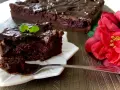 Pyszny brownie z wiśniami, polane czekoladą, z listkiem mięty. Obok czerwona róża.