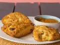 Złociste bułeczki scones z rodzynkami, podane na białym talerzu z dżemem. Idealne na popołudniową herbatkę.