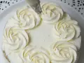 Delikatny tort ozdobiony kremem z białej czekolady w kształcie różyczek. Pyszna słodycz czeka na degustację.
