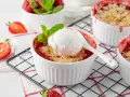 Pyszny crumble z truskawkami w białych kokilkach, ozdobiony świeżymi owocami i miętą.