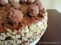 Pyszny tort Ferrero Rocher, oblany czekoladą i obsypany płatkami migdałów, z całymi czekoladkami na wierzchu.