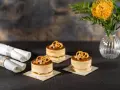 Trzy mini torty z kremem i polewą o smaku słonego karmelu, ozdobione precelkami i orzeszkami. Obok zwinięte serwetki.
