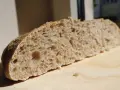 Kromka chleba na zakwasie z widocznymi nierównościami i dużymi dziurami, świadczącymi o błędach przy pieczeniu chleba na zakwasie.