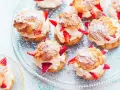 Pyszne ptysie z kremem patissiere i świeżymi truskawkami, posypane cukrem pudrem, prezentują się apetycznie na szklanej paterze.