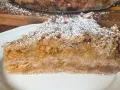 Kawałek pysznego jabłecznika sypanego, posypanego cukrem pudrem, z widocznymi warstwami jabłek i kruszonki.
