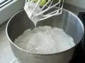 Ubita śmietana z mascarpone, idealne proporcje dla puszystego kremu. Mikser z białą masą w metalowej misie.