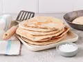 Stos świeżo usmażonych chlebków z patelni, obok miseczka soli i łopatka. Idealne na śniadanie.