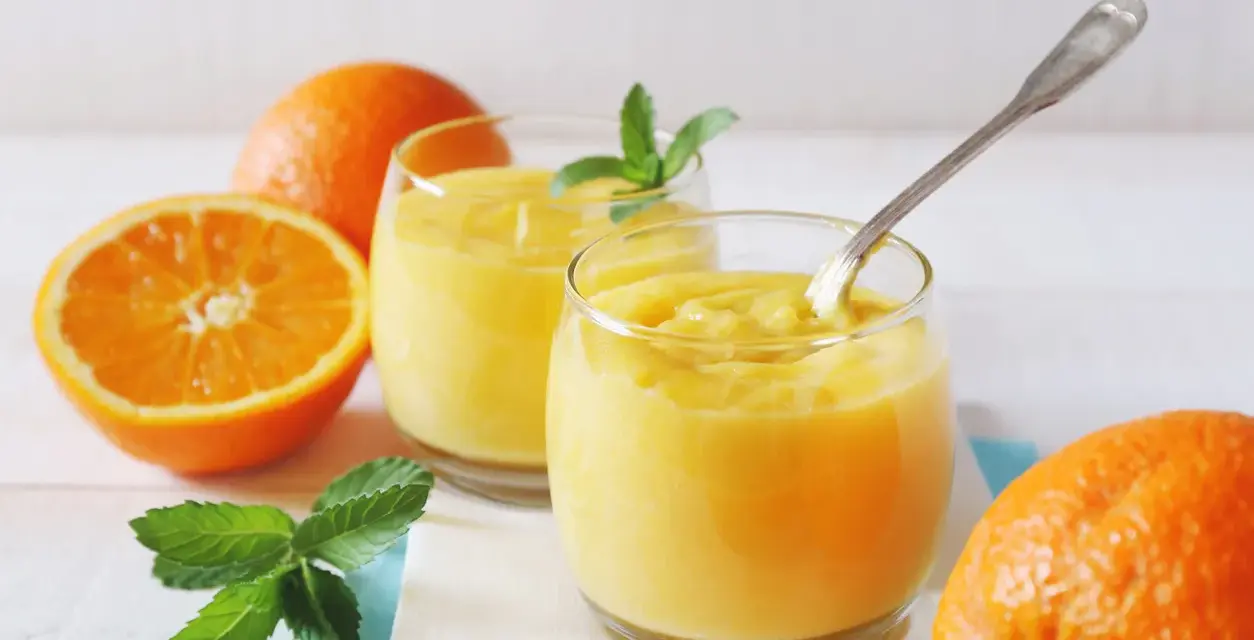 Dwa szklanki orzeźwiającego, gęstego **orange curd** z miętą i świeżymi pomarańczami.