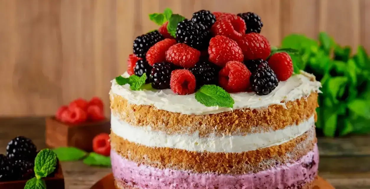 Pyszny tort z warstwami biszkoptu i kremu malinowego, ozdobiony świeżymi malinami, jeżynami i miętą.