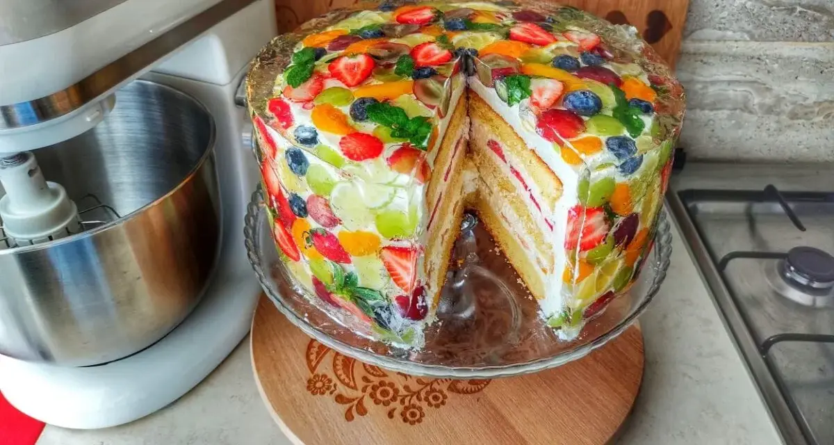 Kolorowy tort z galaretką i owocami, z kawałkiem wyciętym, prezentuje się apetycznie.