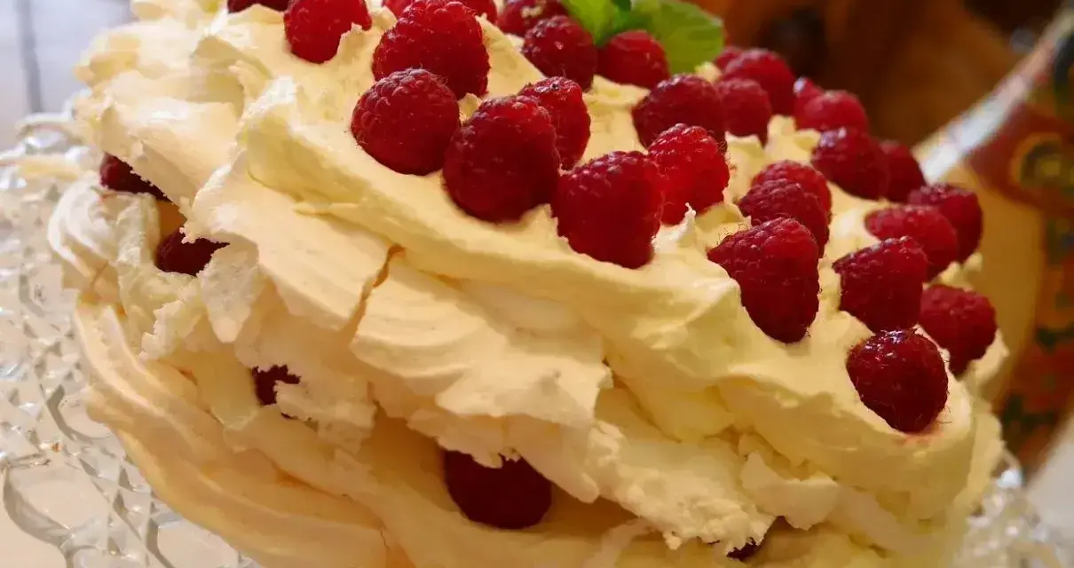 Puszysty, wielowarstwowy tort bezowy z bitą śmietaną i malinami. Wygląda jak najpyszniejszy tort bezowy, jaki można sobie wyobrazić!
