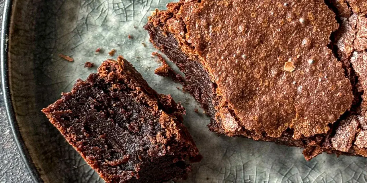 Pyszne, wilgotne brownie bezglutenowe na popękanym, szarym talerzu. Kawałek z widelcem czeka na spróbowanie.