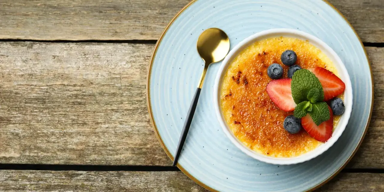 Idealny creme brulee przepis na deser. Karmelizowana skórka, świeże owoce i złota łyżeczka.