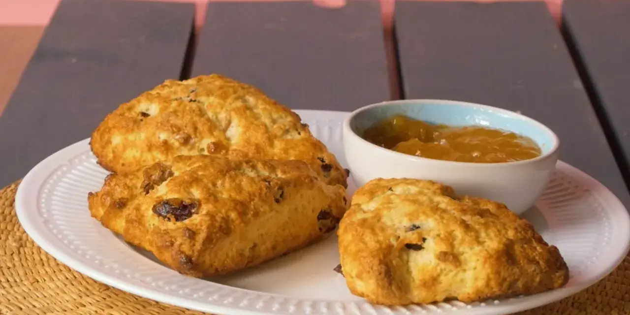 Złociste bułeczki scones z rodzynkami, podane na białym talerzu z dżemem. Idealne na popołudniową herbatkę.