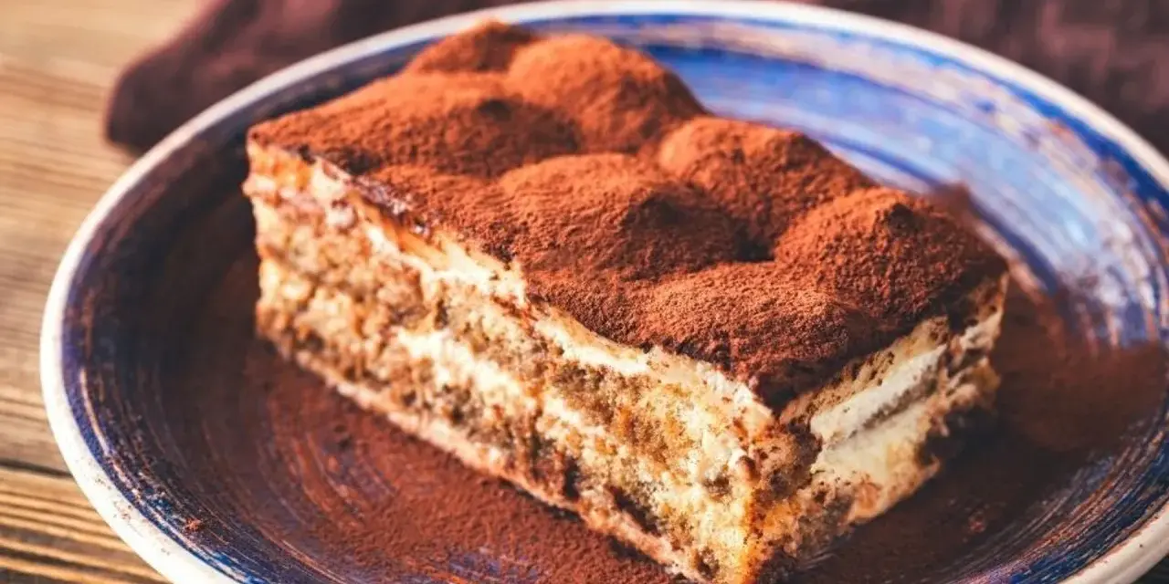 Pyszne tiramisu bez pieczenia, posypane obficie kakao, na niebieskim talerzu. Idealne na deser.