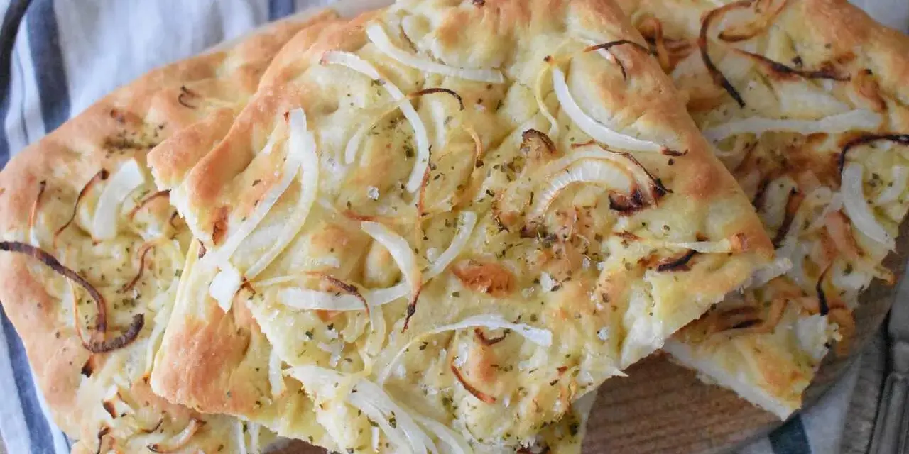 Pyszna focaccia z cebulą, posypana ziołami i solą, prezentuje się apetycznie na drewnianej desce.