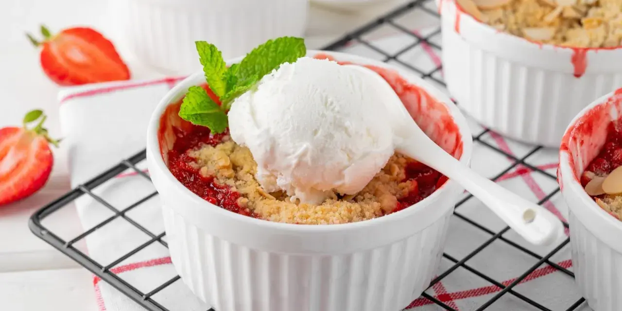 Pyszny crumble z truskawkami w białych kokilkach, ozdobiony świeżymi owocami i miętą.