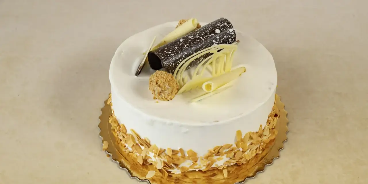 Elegancki tort rafaello z wiórkami migdałowymi, czekoladową rurką i dekoracjami z białej czekolady.
