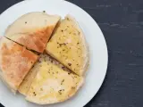 Pokrojone na ćwiartki bolo do caco, posypane ziołami, na białym talerzu.