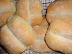 Kilka świeżych, złocistych bułek pszenno żytnich ułożonych na kratkowanej ściereczce.
