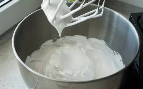 Ubita śmietana z mascarpone, idealne proporcje dla puszystego kremu. Mikser z białą masą w metalowej misie.