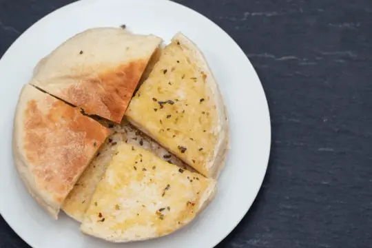 Pokrojone na ćwiartki bolo do caco, posypane ziołami, na białym talerzu.