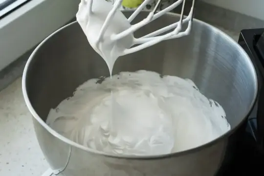 Ubita śmietana z mascarpone, idealne proporcje dla puszystego kremu. Mikser z białą masą w metalowej misie.