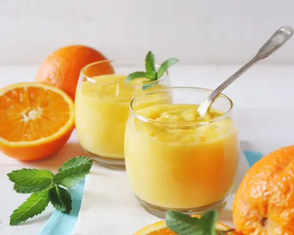 Dwa szklanki orzeźwiającego, gęstego **orange curd** z miętą i świeżymi pomarańczami.