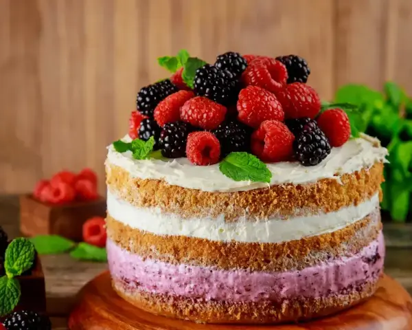 Pyszny tort z warstwami biszkoptu i kremu malinowego, ozdobiony świeżymi malinami, jeżynami i miętą.
