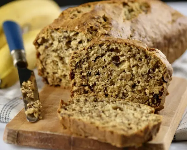 Pyszny chlebek bananowy, świeżo upieczony, z widocznym nożem i bananami w tle. Idealny na śniadanie.