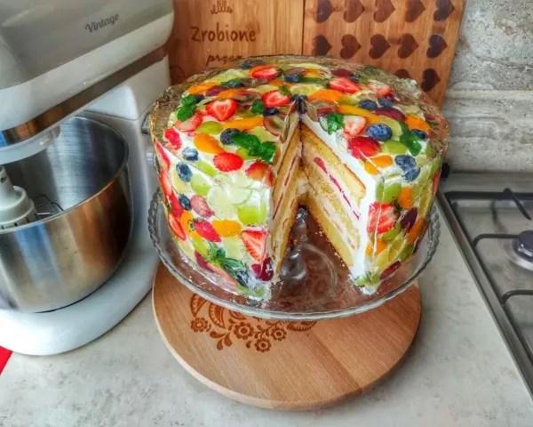 Kolorowy tort z galaretką i owocami, z kawałkiem wyciętym, prezentuje się apetycznie.