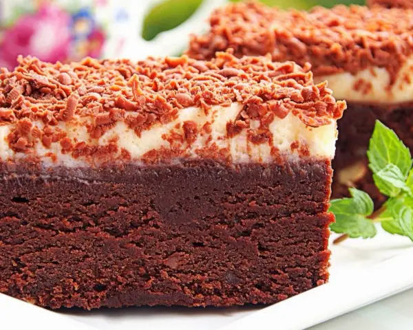 Pyszny torcik brownie z kremową warstwą i posypką czekoladową, ozdobiony listkami mięty.