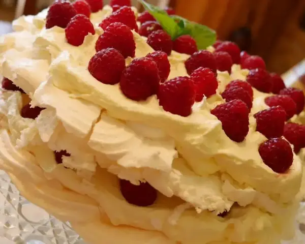 Puszysty, wielowarstwowy tort bezowy z bitą śmietaną i malinami. Wygląda jak najpyszniejszy tort bezowy, jaki można sobie wyobrazić!