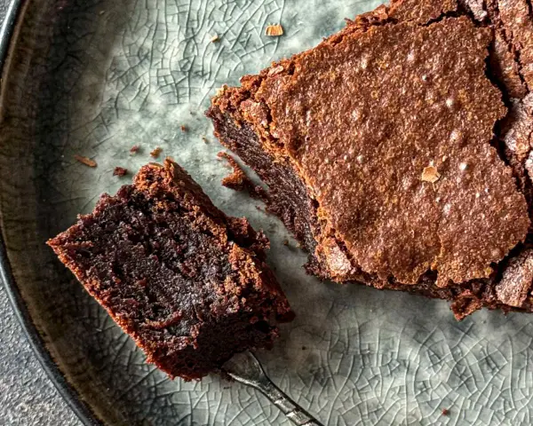 Pyszne, wilgotne brownie bezglutenowe na popękanym, szarym talerzu. Kawałek z widelcem czeka na spróbowanie.