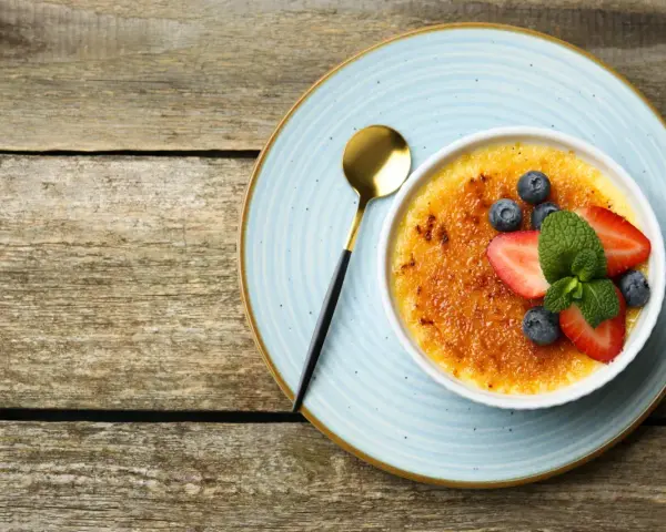 Idealny creme brulee przepis na deser. Karmelizowana skórka, świeże owoce i złota łyżeczka.