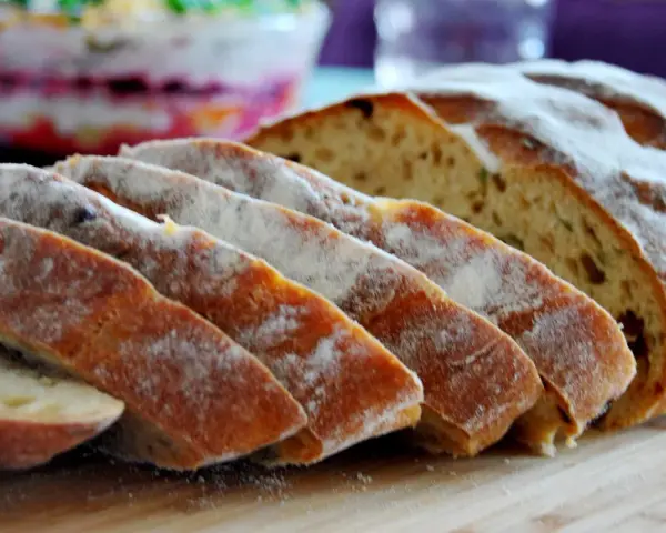 Pokrojony chleb z pomidorami, posypany mąką, leży na desce. W tle widać sałatkę.