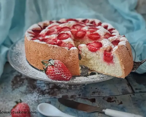 Puszysty biszkopt z truskawkami, posypany cukrem pudrem, kusi apetycznym wyglądem. Idealny na letnie popołudnie.