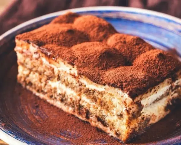 Pyszne tiramisu bez pieczenia, posypane obficie kakao, na niebieskim talerzu. Idealne na deser.