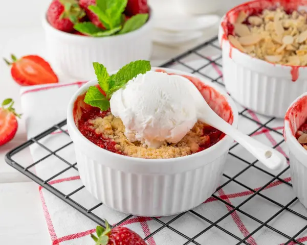 Pyszny crumble z truskawkami w białych kokilkach, ozdobiony świeżymi owocami i miętą.