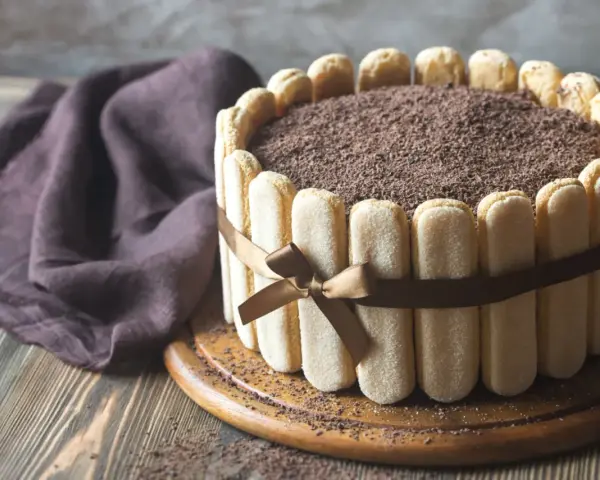 Wykwintny tort tiramisu, otoczony biszkoptami i ozdobiony czekoladową posypką, prezentuje się apetycznie.