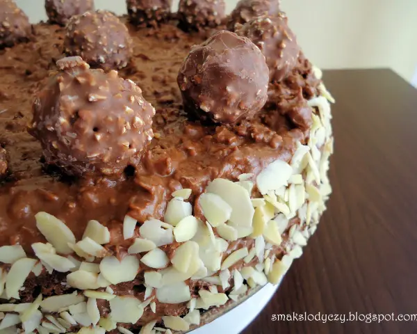 Pyszny tort Ferrero Rocher, oblany czekoladą i obsypany płatkami migdałów, z całymi czekoladkami na wierzchu.