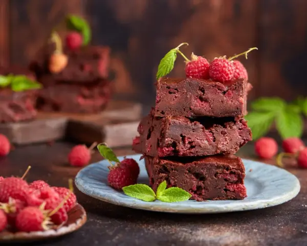 Stos pysznych brownie z malinami, ozdobiony świeżymi malinami i listkami mięty.