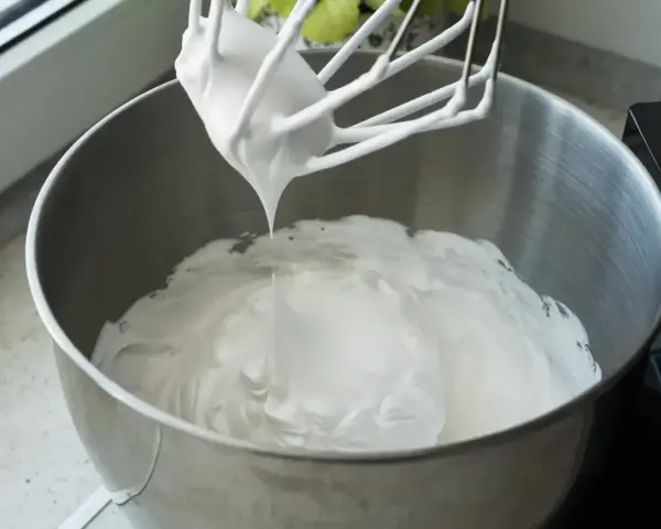 Ubita śmietana z mascarpone, idealne proporcje dla puszystego kremu. Mikser z białą masą w metalowej misie.