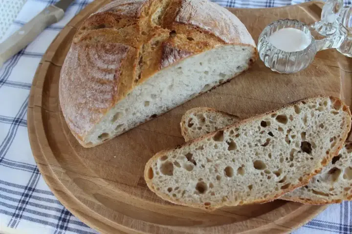 Chleb nocny na zakwasie, pokrojony na desce, z widocznym puszystym wnętrzem i chrupiącą skórką. Obok mała miseczka z solą.